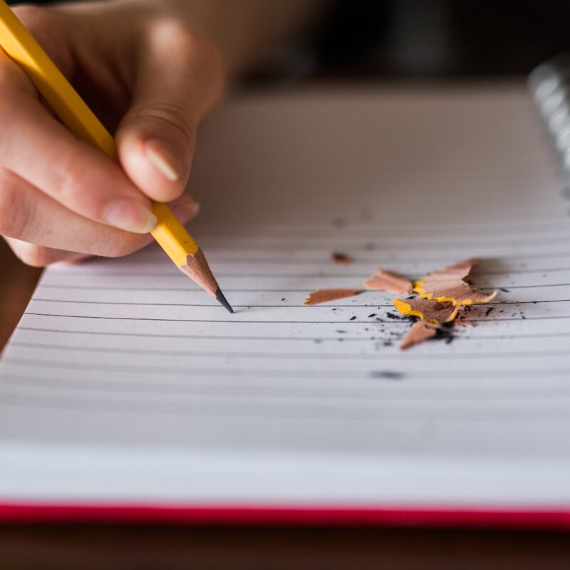 person holding pencil writing on notebook