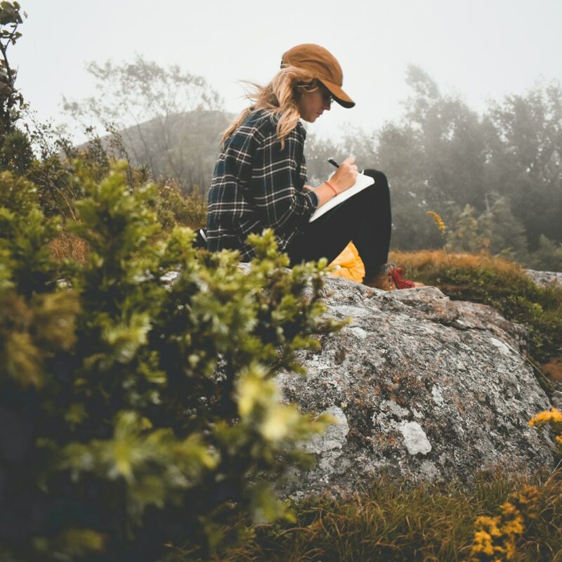 a woman sitting on top of a rock writing